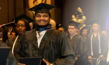 Herzing University online MBA graduate smiling while walking to receive his degree